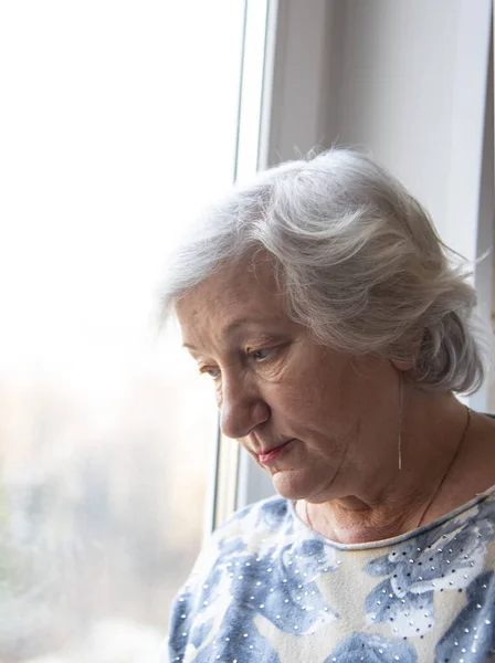 Vertikales Porträt einer älteren Frau am Fenster. — Stockfoto