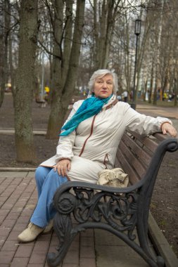 Parktaki bankta oturan zarif, yaşlı, gri saçlı bir kadın..