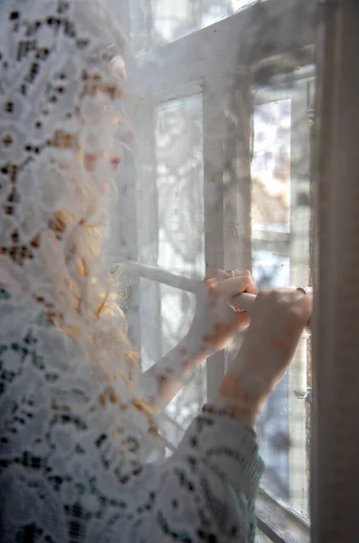 Die Silhouette eines Mädchens, das hinter einem Spitzenvorhang steht und aus dem Fenster schaut. — Stockfoto