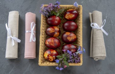 Paskalya kompozisyonu, gri arka planda renkli Paskalya yumurtaları ve keten peçetelerle dolu bir sepet..