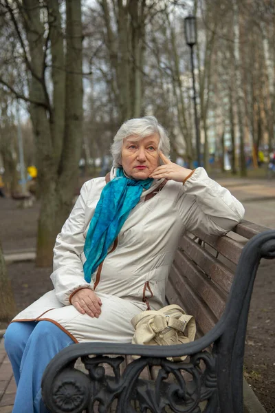 春の初めに公園のベンチに座っている上品なお年寄りの白髪の女性 — ストック写真