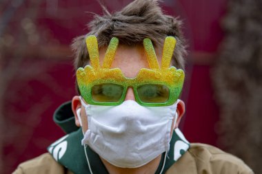 Koruyucu tıbbi maskeli ve komik güneş gözlüklü genç bir adamın portresi. Koronavirüs salgını durumunda önleyici önlemler.