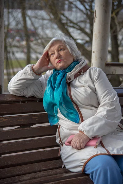 彼女の手にピンクの財布と公園のベンチに座っている悲しい高齢者の女性 — ストック写真