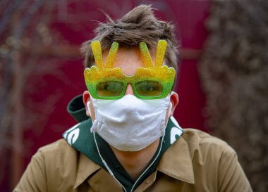 Koruyucu tıbbi maskeli ve komik güneş gözlüklü genç bir adamın portresi. Koronavirüs salgını durumunda önleyici önlemler.