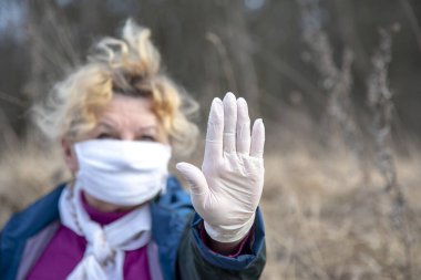 Tıbbi koruyucu maske ve lastik eldiven takan yaşlı bir kadın koronavirüsü durdurur. Coronavirüs salgınının sonunu sembolize eden konsept fotoğraf. Eldivenli ele odaklan..