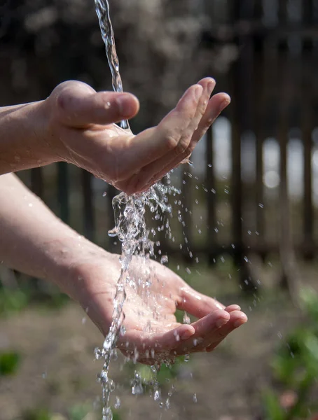 Strong male hands under a stream of water on a blurred natural background.