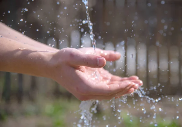 Strong male hands under a stream of water on a blurred natural background.