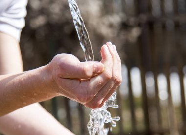 Genç bir adamın eli bulanık bir zeminde berrak bir su akıntısının altında..