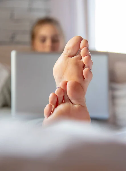 Concéntrate en los pies en primer plano. Una adolescente está acostada en una cama con un portátil . — Foto de Stock