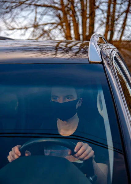 Un joven con una máscara médica está sentado al volante de un auto. . — Foto de Stock