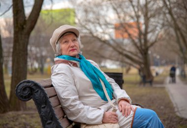 Zarif giyimli yaşlı bir kadın bir ara sokakta bankta oturuyor..