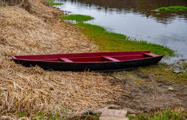 Um barco de madeira vermelho está amarrado na margem do rio . — Fotografia de Stock