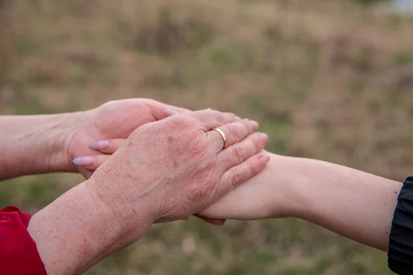 The hand of a young girl in the elderly hands of her grandmother on a blurred background of nature. Conceptual family photo, continuity of generations.