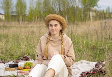 Şapkalı genç bir kız battaniyenin üzerinde oturuyor. Çimlerin üzerinde piknik. Sağlıklı beslenme.