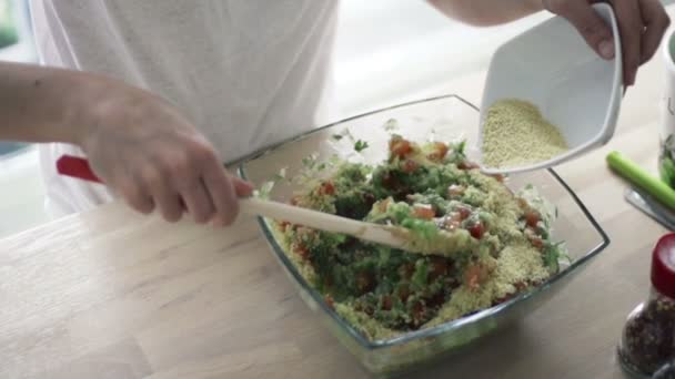 Женщина смешивает салат с деревянной ложкой и добавляет кускус каша замедленной съемки — стоковое видео