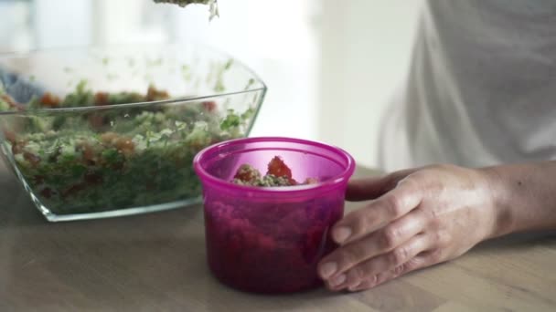 Женщина кладет салат в пластиковую коробку на кухне — стоковое видео