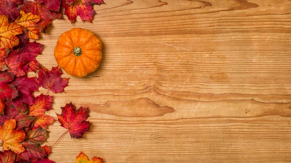 Un fond en bois avec feuillage d'automne et une citrouille — Photo