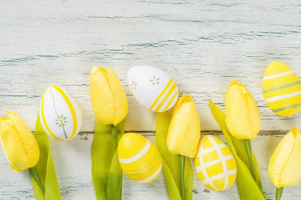 Ovos de páscoa amarelos com tulipas em um fundo rústico branco — Fotografia de Stock