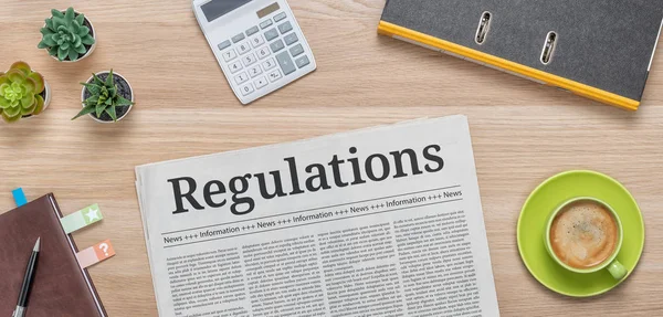 A newspaper on a desk with the headline Regulations — Stock Photo, Image
