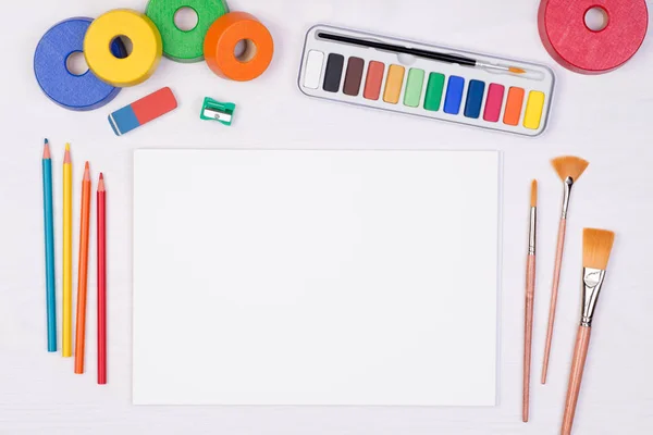 在儿童书桌上有彩色铅笔 刷子和水彩的白纸 上面有复制空间的视图 — 图库照片