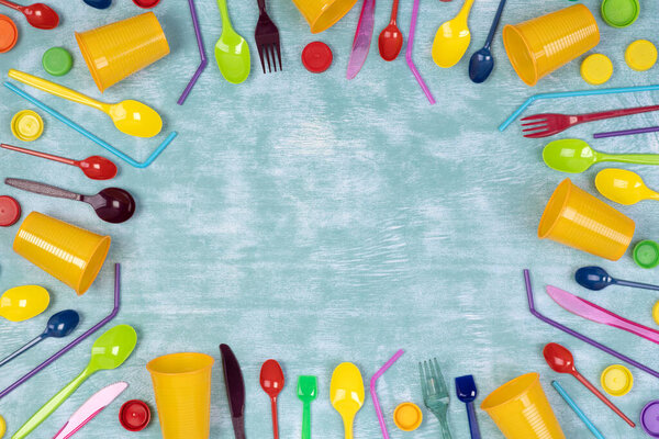 Disposable single use plastic objects such as cups, forks and spoons and drinking straws on blue background with copy space