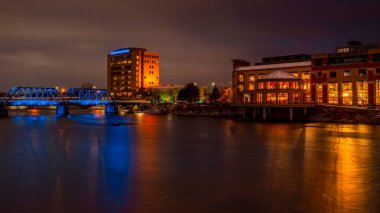 Grand Rapids, Ortaçağ 14, 2019; Grand Valley State binasından gelen turuncu ve mavi ışık, halk müzesi ve kiriş köprüsü sabah erken saatlerde Grand River 'dan yansıyor.