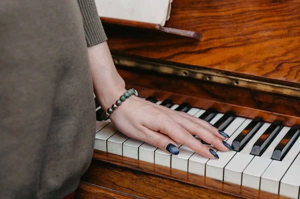 The hand of a young woman lies on the keys of a piano