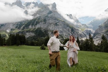 mutlu gelin gelinlik ve elele ve bulutlar ile Alpin çayır üzerinde yürüyen damat