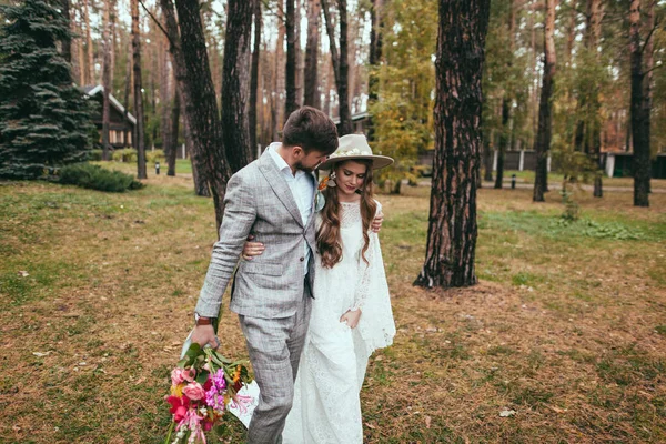 ハグと森を歩く新郎新婦のウェディング ドレスの美しい花嫁 — ストック写真