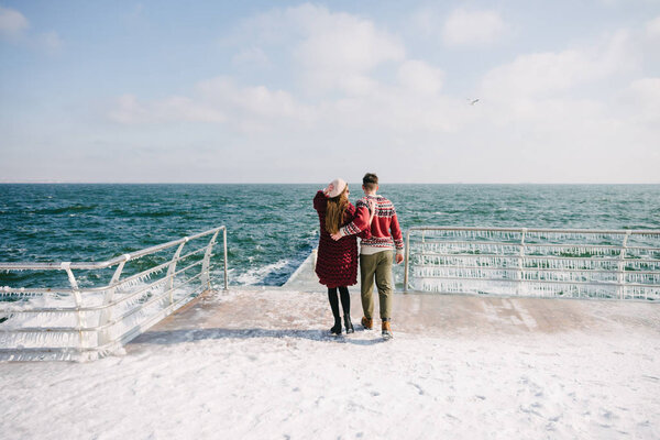 back view of stylish couple hugging on quay near sea