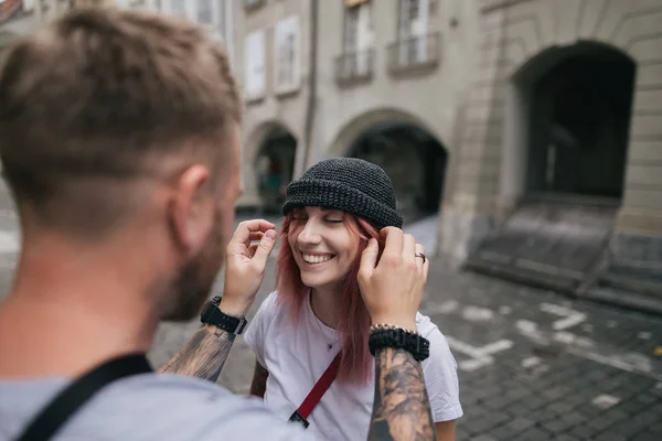 Messa a fuoco selettiva di uomo mettendo cappello sulla bella giovane donna sorridente mentre camminano insieme per strada a Berna, Svizzera — Foto stock