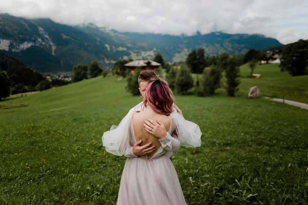 Rückansicht von Braut und Bräutigam, die sich auf der grünen Bergwiese in den Alpen umarmen — Stockfoto