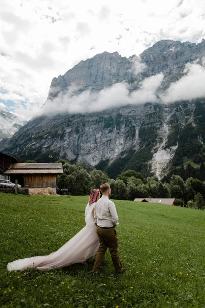 Noiva jovem e noivo andando no prado da montanha verde com nuvens nos Alpes — Fotografia de Stock