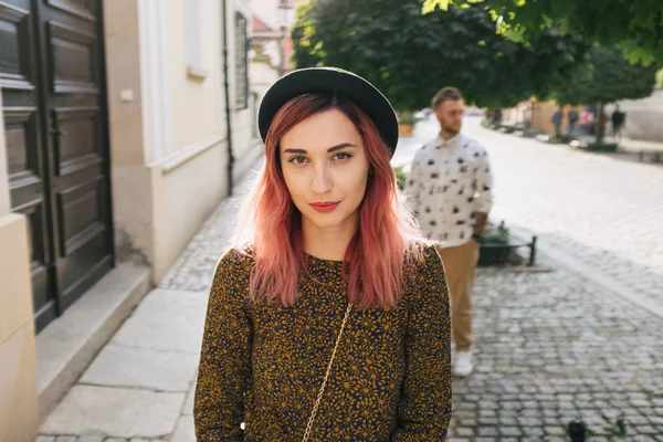 Hermosa chica elegante con el pelo rosa mirando a la cámara, novio de pie detrás - foto de stock
