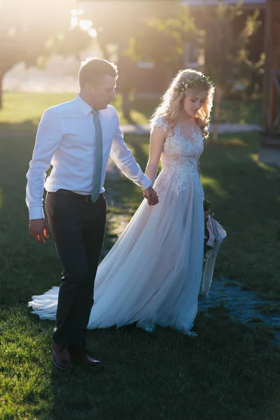 Beautiful young wedding couple holding hands and walking in green lawn — Stock Photo