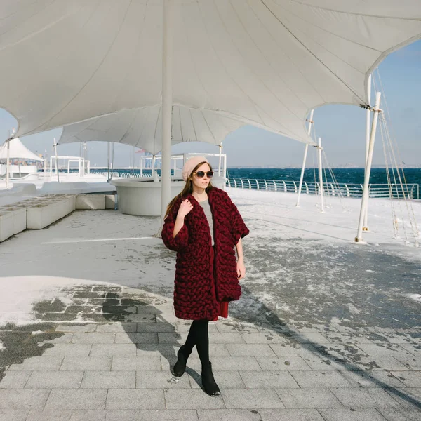 Beautiful girl in sunglasses and burgundy merino wool cardigan walking on quay — Stock Photo