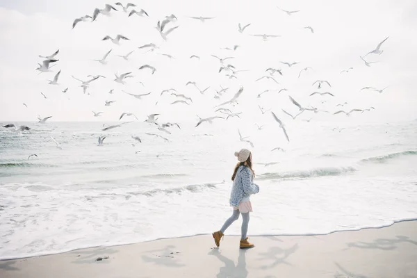 Stylisches Mädchen läuft mit Möwen über winterliches Meer — Stockfoto