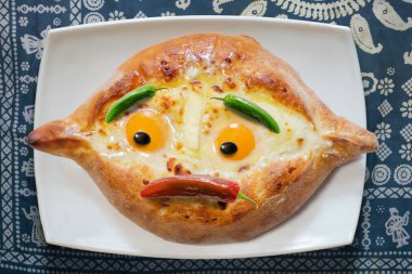 Gürcü çanak Acara khachapuri plaka, mavi tableclothe arka plan üzerinde üzgün yüz ile yumurta ile,