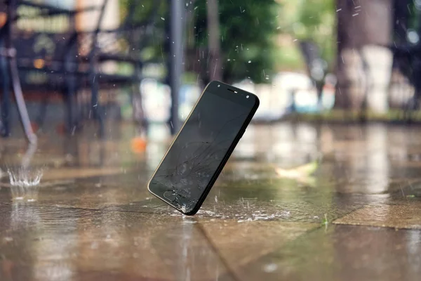 Smartphone faller och kraschar på våt mark i stadsparken — Stockfoto