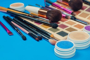 Mavi bir yüzeyde makyaj ürünleri, fırçalar ve paletler