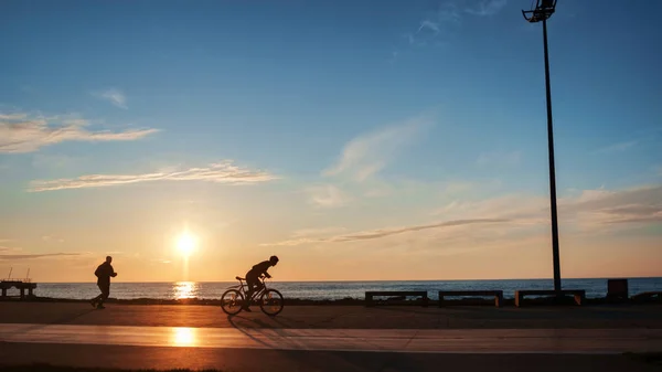 Sylwetki biegacza i rowerzysty w parku o zachodzie słońca — Zdjęcie stockowe