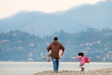 Baba çocuklarıyla yürüyüşe çıkıyor. Deniz kenarında garip bir yol, seçici bir odaklanma.