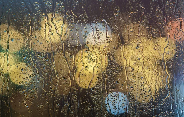 Flowing rain drops on the wet  window glass, blurred illuminated background