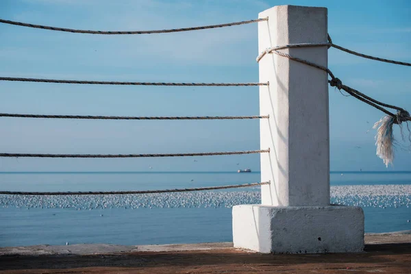 White concrete and rope barrier on the pier with blue sky and sea background