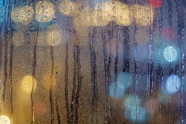 Islak cam pencereye yoğunlaşma ve bardaktan boşanırcasına akan yağmur damlaları, bulanık arka plan