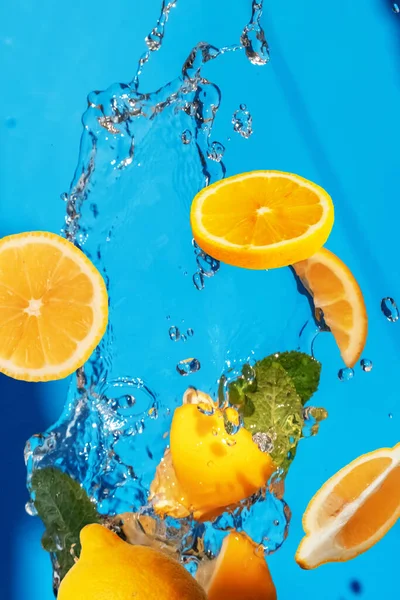 Falling fresh slices of the lemon with fresh water in the air. Flying fruits concept on blue background