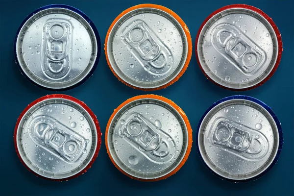 Color shiny metallic drink cans with water drops on dark blue background, top view