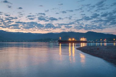 Rıhtımın gündüz freninde liman manzarası. Geminin ışıkları sakin denizi yansıtıyor
