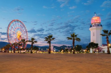 Deniz feneri ve dönme dolabı olan büyük bir kaldırım şafakta mavi bulutlu arka planda.
