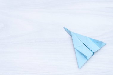 Flat lay of blue paper plane on white wooden background. Copy space. Travel concept.